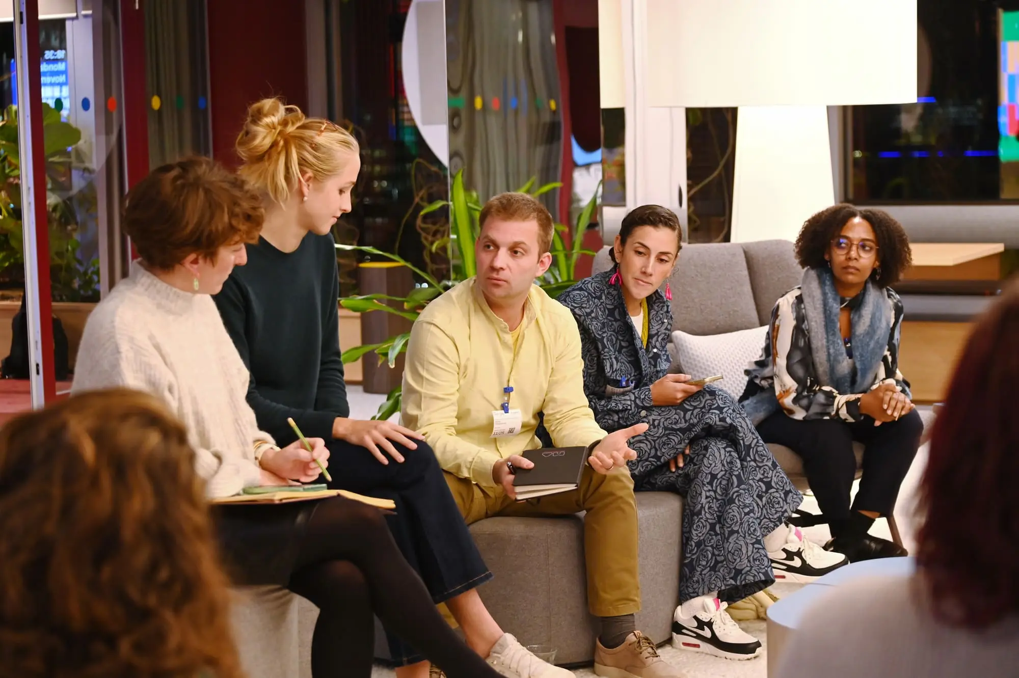A small mixed group in discussion on sofas at a Next Women gathering, some taking notes